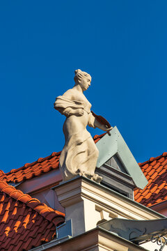a bright white statue of a lady standing on the top of the roof in the old town of Torun