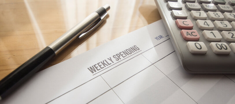 weekly expense sheet printed on the table. Calculator , pen and weekly spending on the desk.