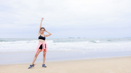 asian woman wearing sportwear and pink jacket exercise and relax on the sea beach at evening in the rain season