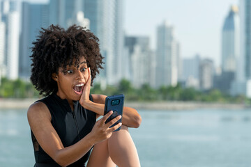 Cheerful latina afro woman with surprise gesture during video call through smartphone  - stock photo