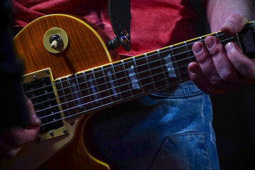 Fototapeta premium A guitarist in jeans plays the guitar in a dark room. Hands of a Guitar player playing the guitar. Selective focus. Soft focus