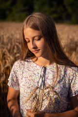 Fototapeta premium Portrait of a girl with some spikelets in the field of ripe grain. Portrait of beautiful teenage girl