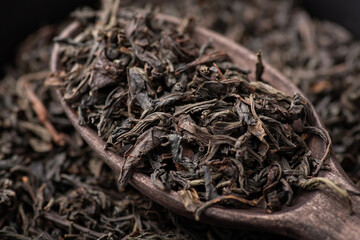 Black dried tea leaves in wooden spoon. Close-up shot of tea