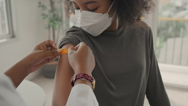 A female doctor is applying plaster to a child's shoulder after being vaccinated. Children wear face masks. Opening sleeves to vaccinate against flu or epidemic in health care and vaccinated concept.