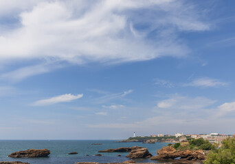 Fototapeta na wymiar Sea surface of Biscay Bay, rocks formed by it, the Biarritz coastal line with a lighthouse. Biarritz, French Basque Country