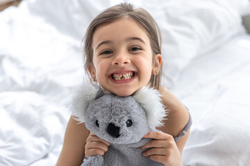 Happy little girl with soft toy koala in bed. © puhimec