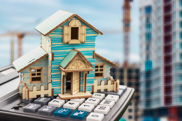 Model of a house on a calculator on the background of a construction site. Real estate mortgage concept. Buying or building a new home, insurance, rent. copyspace.