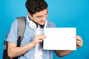 Hispanic teenager college student looking at sheet of paper with copy space isolated on blue background