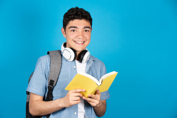 Portrait of hispanic college student holding a book isolated on blue background.