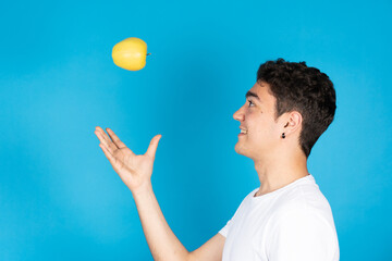 Hispanic young man throwing apple to air and playing with fruit isolated on blue background