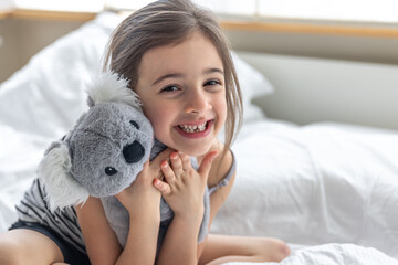 Happy little girl with soft toy koala in bed. © puhimec