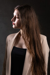 Portrait of a young brunette with long hair in the studio. Dramatic photo in dark colors.