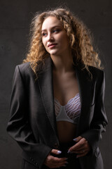 Portrait of a young red-haired curly sexy girl in a jacket with long hair in the studio. Shows off her curvaceous breasts in a bra.