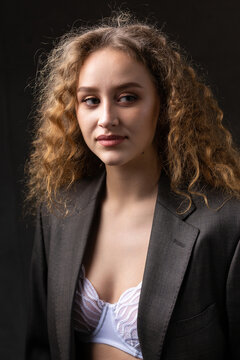 Portrait of a young red-haired curly sexy girl in a jacket with long hair in the studio. Shows off her curvaceous breasts in a bra.