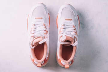 White women's sneakers with coral inserts on white concrete background. Top view. Flat lay.