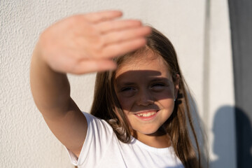 Fashion kid concept - portrait of a girl covering her face from the bright sun while standing...