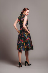 Cut out waist midi dress in floral embroidery with black high heels. Ginger lady walking in studio. Evening colourful elegant gown with high neck line, female fashion, gorgeous chic look.