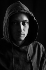 Black and white portrait of a young man with a hood covering his head who in the shadow has a serious and determined look