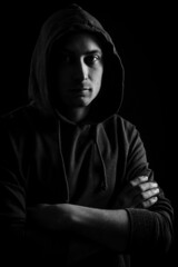 Black and white portrait of a handsome young blue-eyed hooded man with his arms crossed