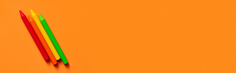 top view of colorful crayons on orange background, banner.