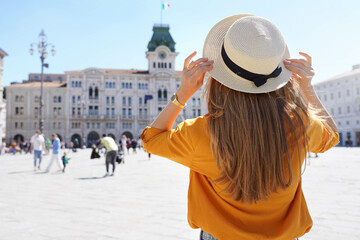 Tourism in Europe. Back view of pretty girl holding hat in Trieste, Italy. Beautiful young woman...