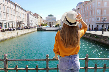 Tourism in Italy. Back view of pretty girl holding hat in Trieste, Italy. Beautiful young woman...
