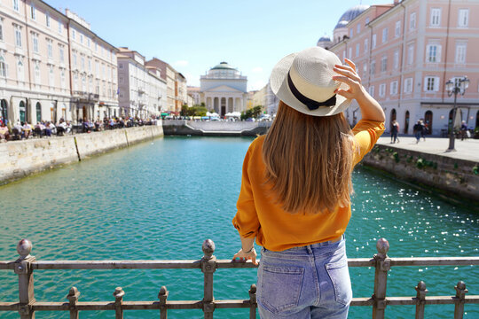 Tourism in Italy. Back view of pretty girl holding hat in Trieste, Italy. Beautiful young woman visiting Europe.