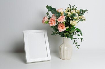 Blank frame mockup in white interior with copy space for photo and fresh roses bouquet