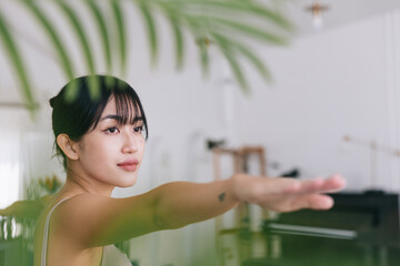 Young smiling attractive sporty Asian woman practicing yoga, doing Virabhadrasana 2 exercise, meditating in Warrior 2 pose, indoor working out at home, wearing sportswear. Half-length body shot.