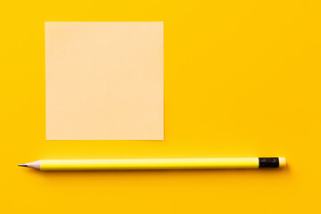 top view of sharp pencil near blank paper note on yellow.