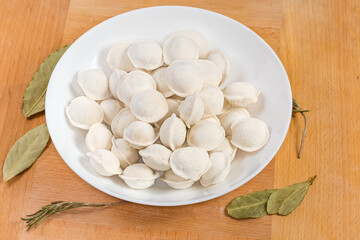 Uncooked frozen meat dumplings on dish on a wooden surface