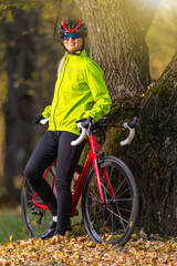 Obraz premium Road Cycling Ideas. Cute Caucasian Female Cyclist With Road Bike Posing Outdoors Near Old Tree Against Autumn Background.