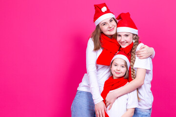 Conceptual Lifestyle. Three Happy Caucasian Girls Wearing Santa Hats Having Fun Together While Cuddling To Each Other Over Trendy Vivid Pink Background
