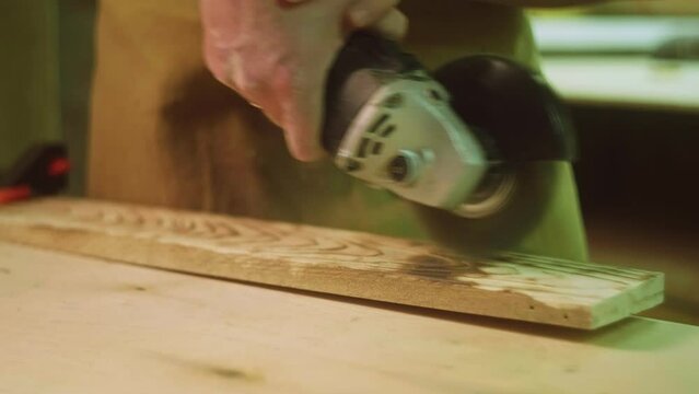 A mature carpenter makes works in his carpentry workshop, grinds wood with a brush