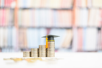 Tuition payment or tuition fee or expense for graduate study abroad program concept : Black graduation cap on stacks of coins, depicts fees charged by education institution for instruction or services - obrazy, fototapety, plakaty