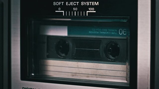 Audiocassette rotates in deck of old tape recorder. Audio cassette with blank label in retro player spinning and playing. Close-up. Retro call recording, playback, reel playing, vintage technology