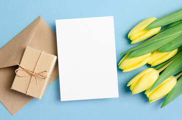 Greeting card mockup with gift box and yellow tulip flowers on blue