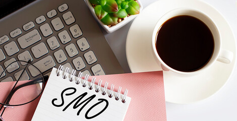 Office supplies, devices, coffee and glasses on white table with text SMO
