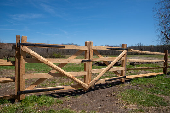 A brand new split rail wooden fence gate in a sunny pasture