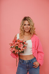 Young beautiful blonde woman with flowers on pink background
