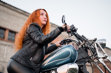 Plakat Red-haired curly woman in leather clothing motorcycle outdoors.