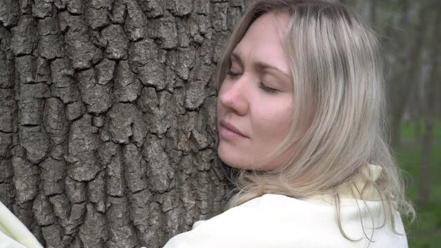 Young woman hugging a tree outdoors. A man presses his face against a tree, the concept of ecology and unity with nature