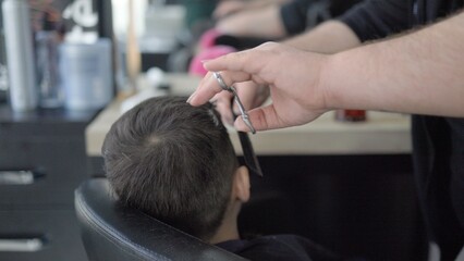 The hairdresser cuts the little boy's hair with scissors. Child in salon