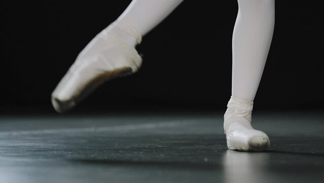 Close-up female legs in white tights and punts of ballet shoes doing dance exercises pulling stretching foot unrecognizable ballerina rehearsing choreography performing on stage in dancing hall