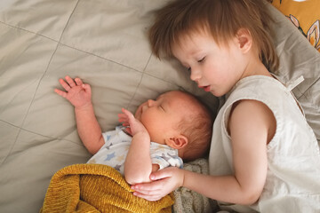 cute chubby baby sleeps on bed next to an older sibling, children are siblings together. older...
