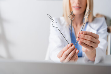 Cropped view of tools in hands of blurred speech therapist working near laptop in consulting room.