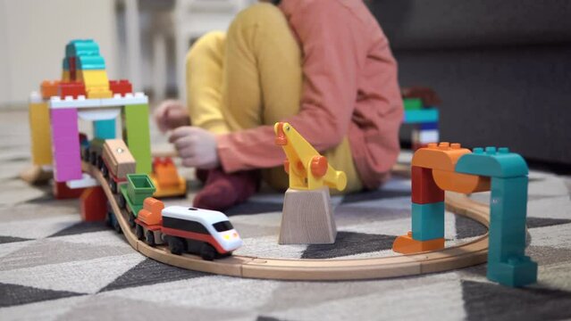 A little boy is playing with a children's railway. The child plays with toys on the floor. Railway bridge from a children's designer. A toy train rides on a wooden railroad.