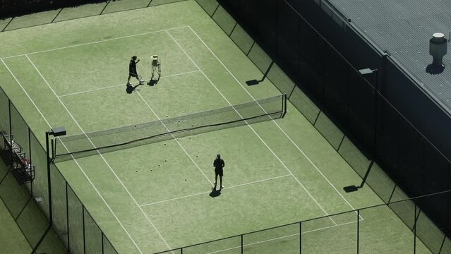 Tennis coach playing volleys to practicing tennis player on lawn grass surface.