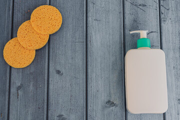 Zero waste concept, sustainable lifestyle. Flat lay with reusable sponge for make-up remover, cosmetic hygiene product in white bottle on blue wooden background. Top view, copy space.