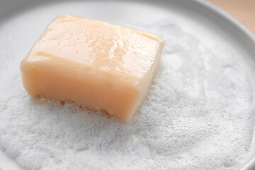 Peach orange pink color soap bar square shape with foam bubbles water on white plate